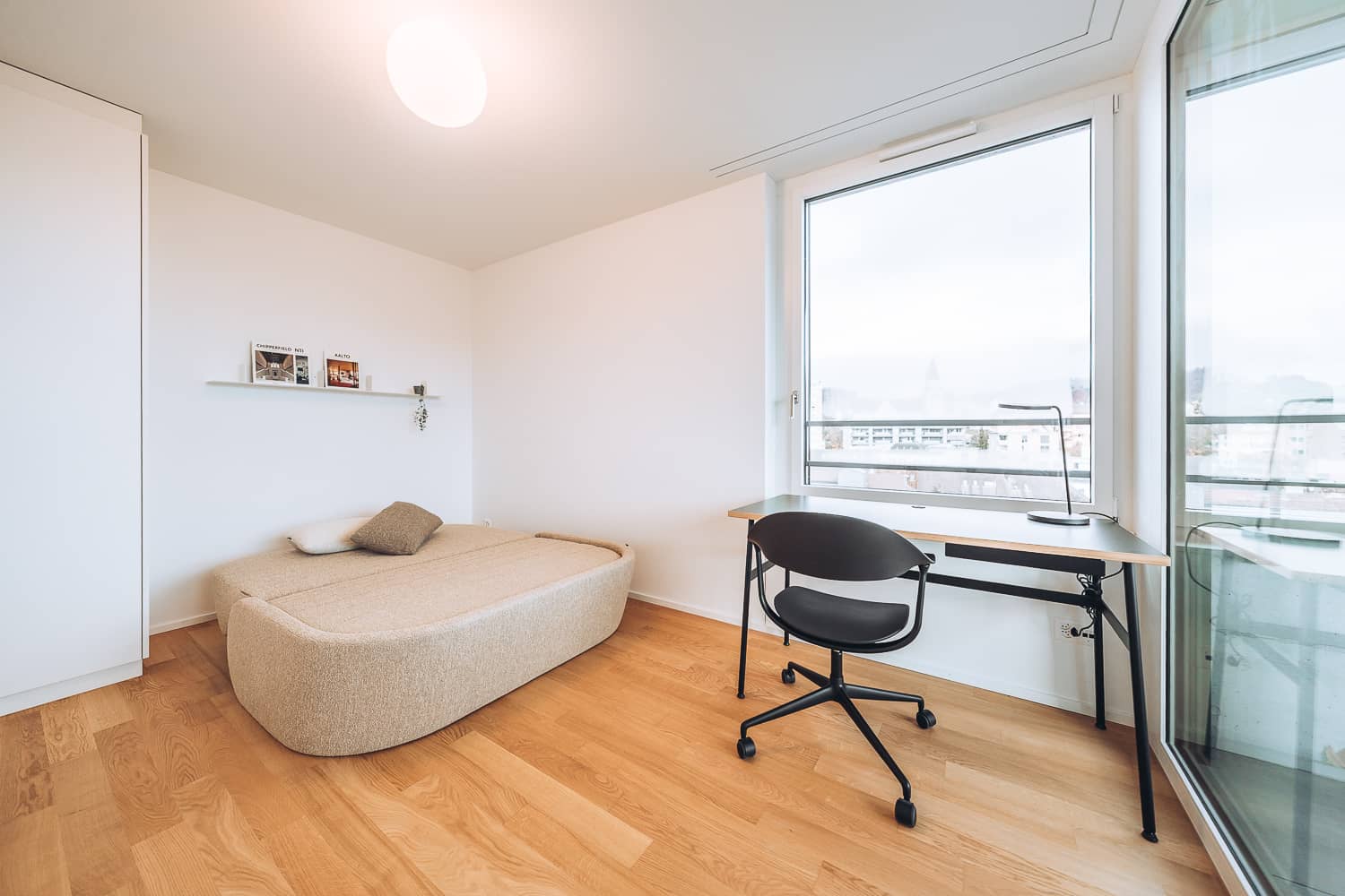 Neben einem Arbeitstisch steht ein ausgezogenes Schlafsofa